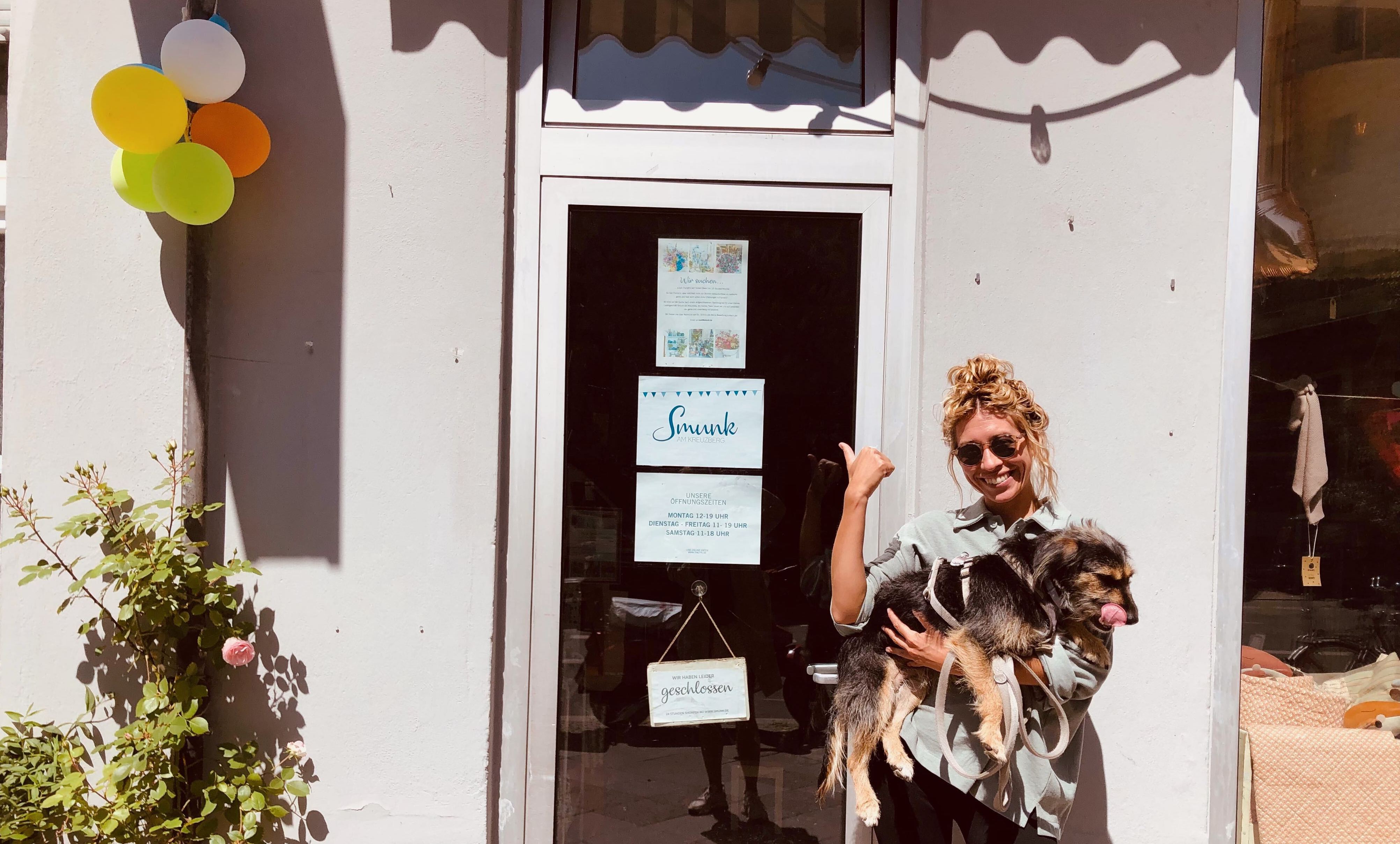 Leonie von nebenan.de steht mit ihrem Hund auf dem Arm vor ihrem Lieblingsladen 